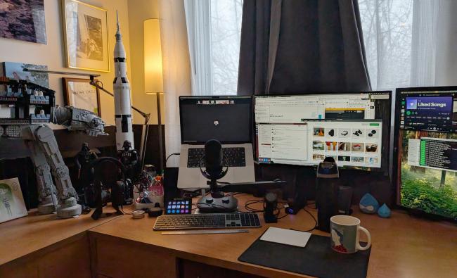 A desk covered in computer and audio tech, with some Star Wars toys in the back